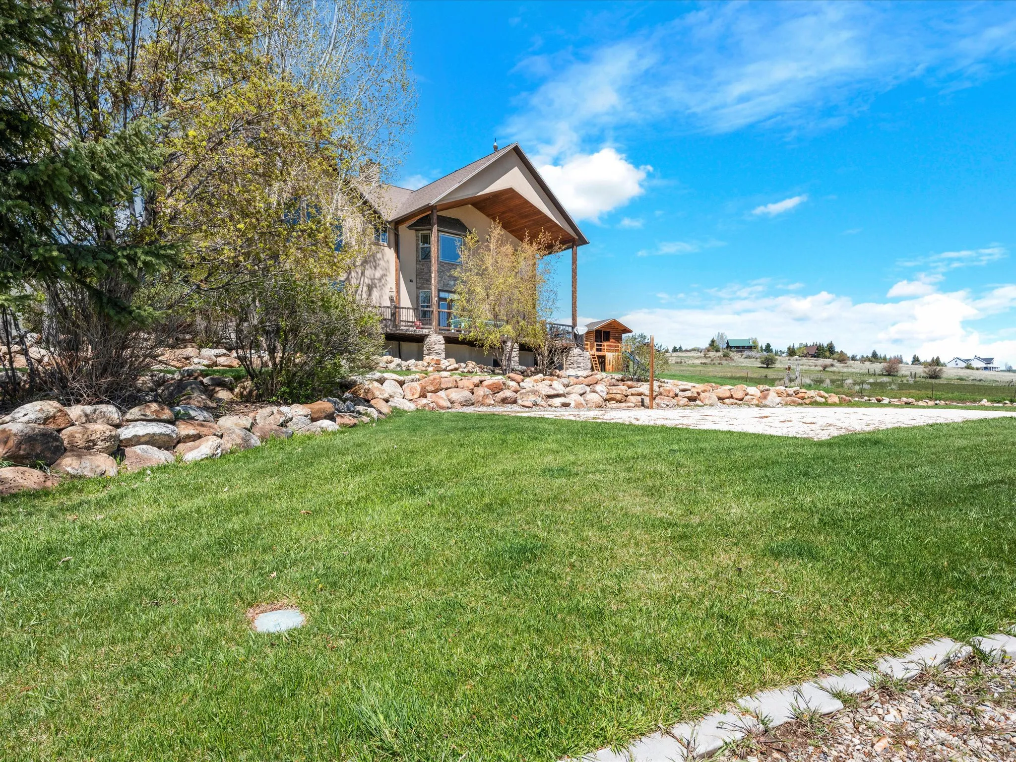 Expansive lawn with a decorative rock wall, mature landscaping, and a multi-level deck