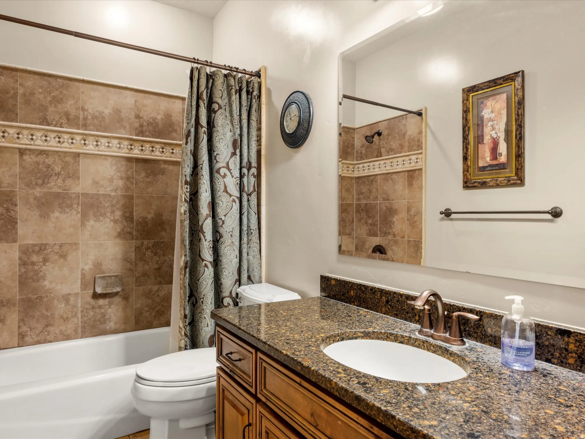 Main floor bathroom.  Bathroom featuring a white bathtub, decorative tile surround with accent band, bronze-finish fixtures, a vanity with a granite countertop, and wood cabinetry