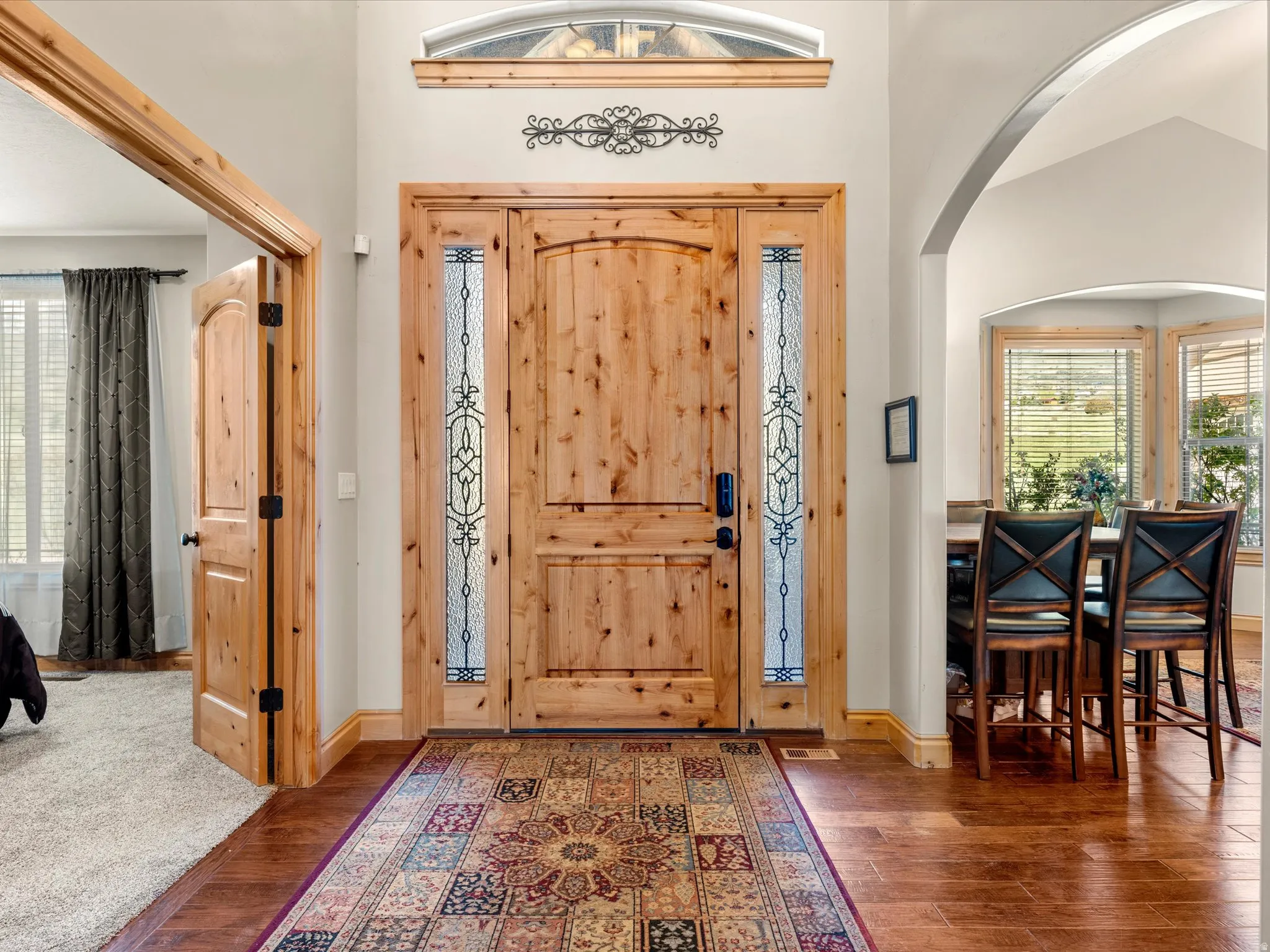 Natural wood entry door with decorative glass sidelights, transom window, wood-finish flooring, and arched entryway