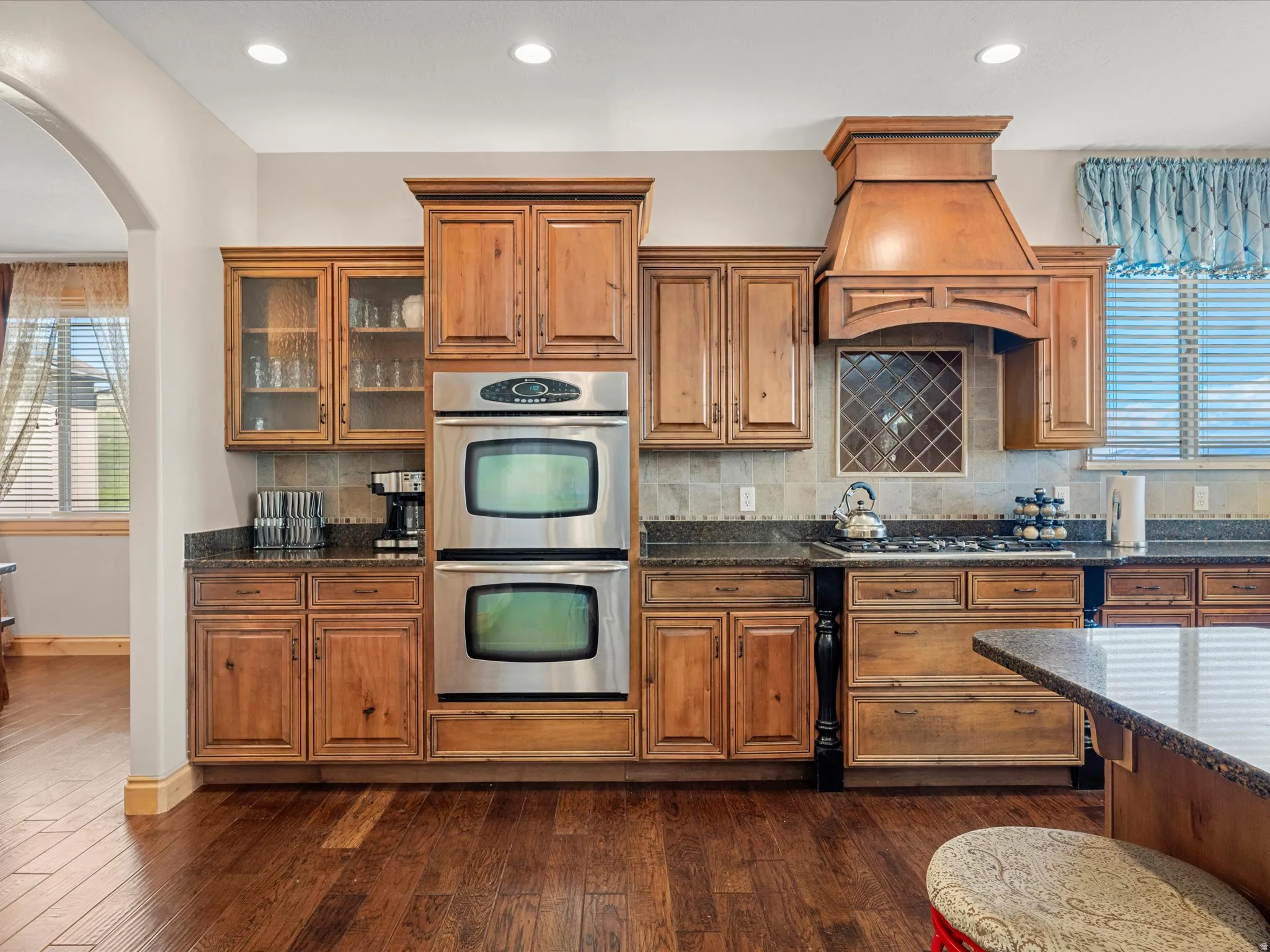 Kitchen featuring a built-in double oven, wood-finish cabinetry, tile backsplash, dark countertops, and recessed lighting