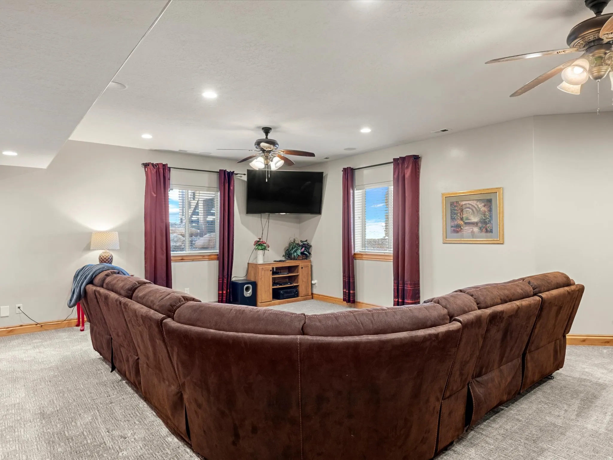 Carpeted living area featuring recessed lighting, a ceiling fan, and multiple windows with wood trim