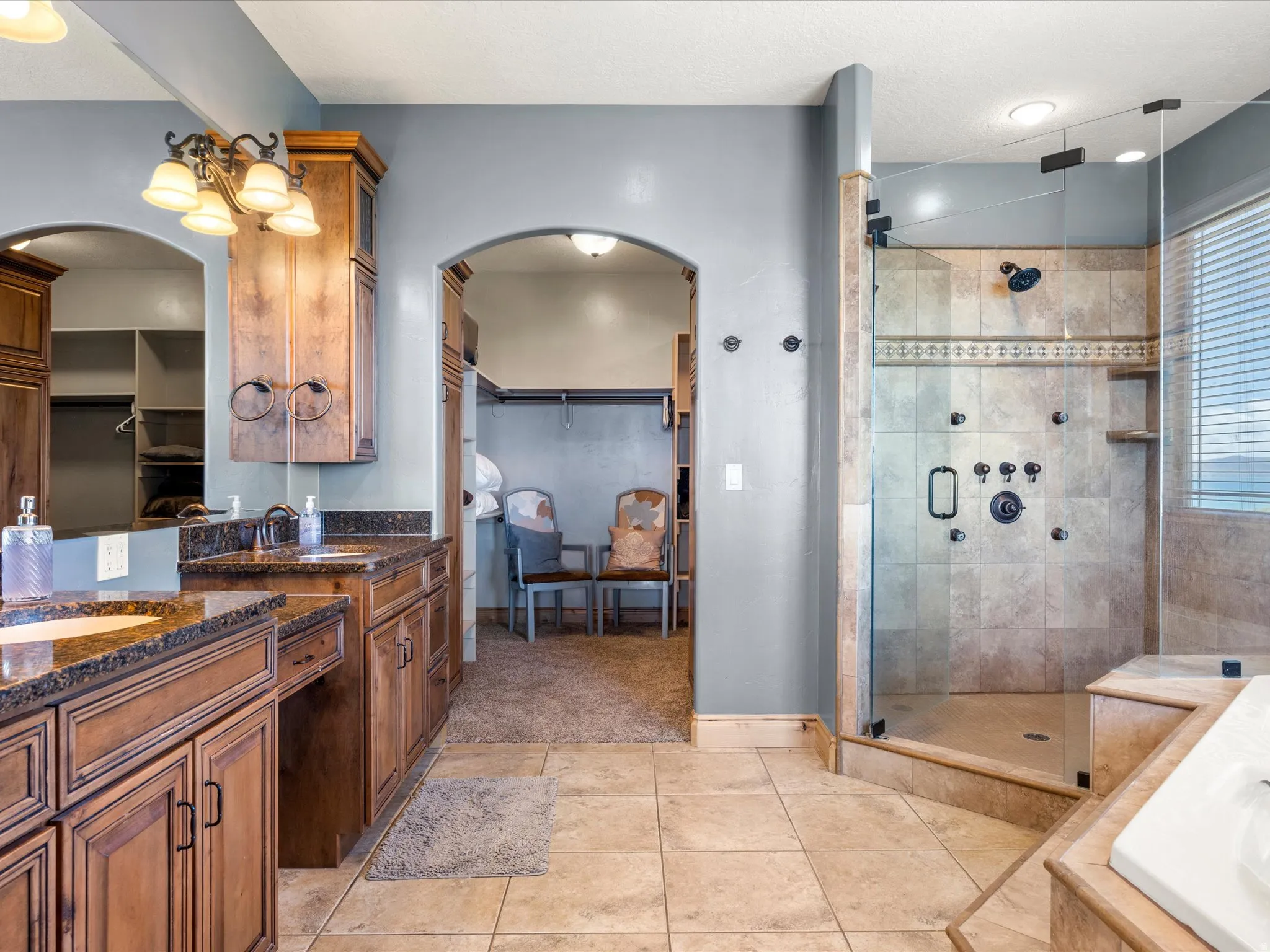 Spacious bathroom featuring dual wood-finish vanities with undermount sinks and dark stone countertops