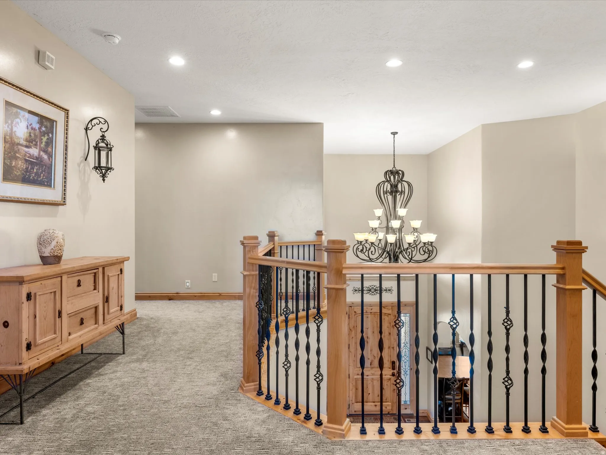 Carpeted hallway featuring a built-in wall sconce, recessed lighting, and a substantial wrought iron chandelier