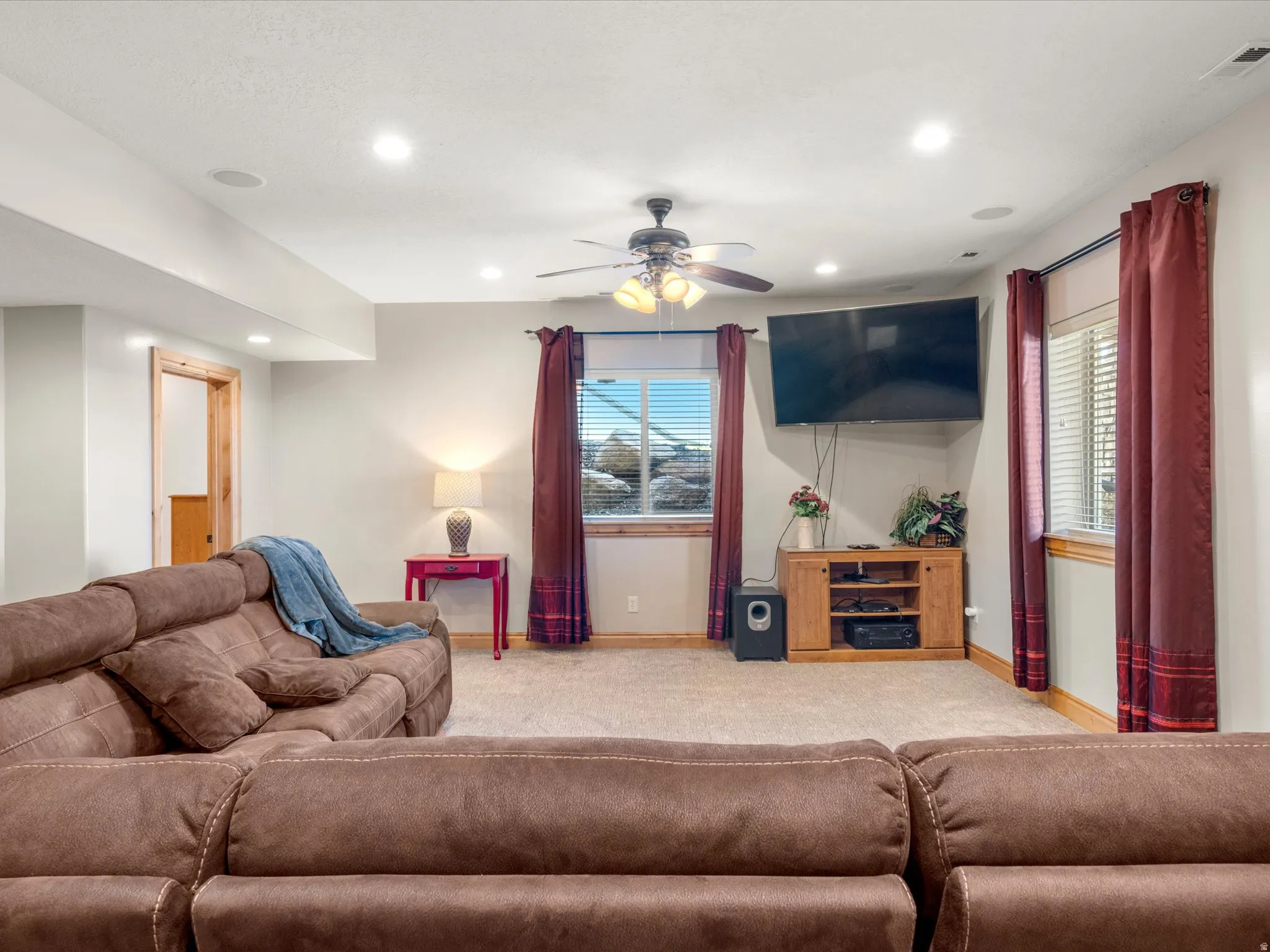 Carpeted entertainment area featuring recessed lighting, a ceiling fan, and two windows with blinds and curtain rods