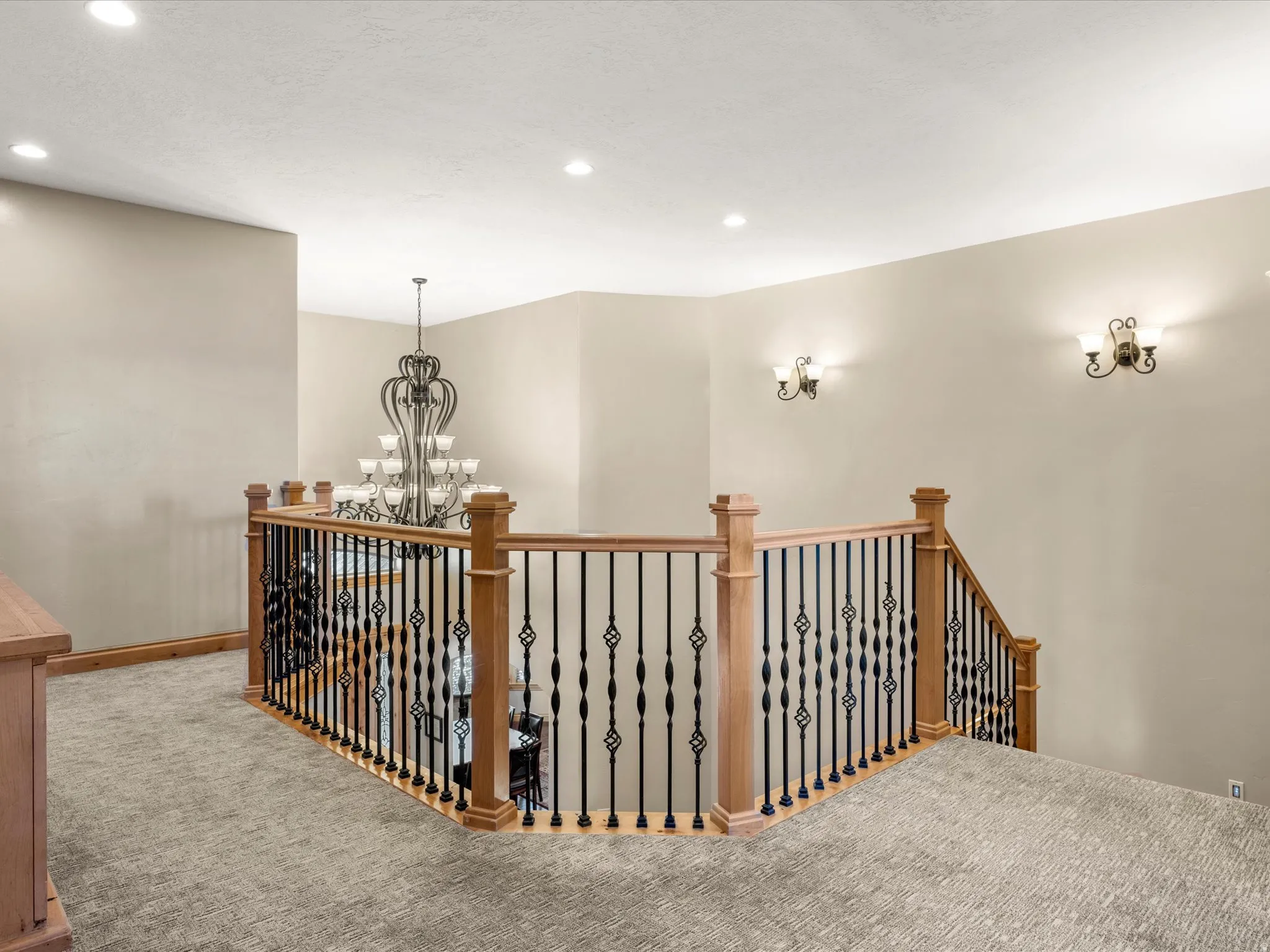Upper-level landing featuring a wood and wrought iron railing, recessed lighting, and wall-mounted sconces