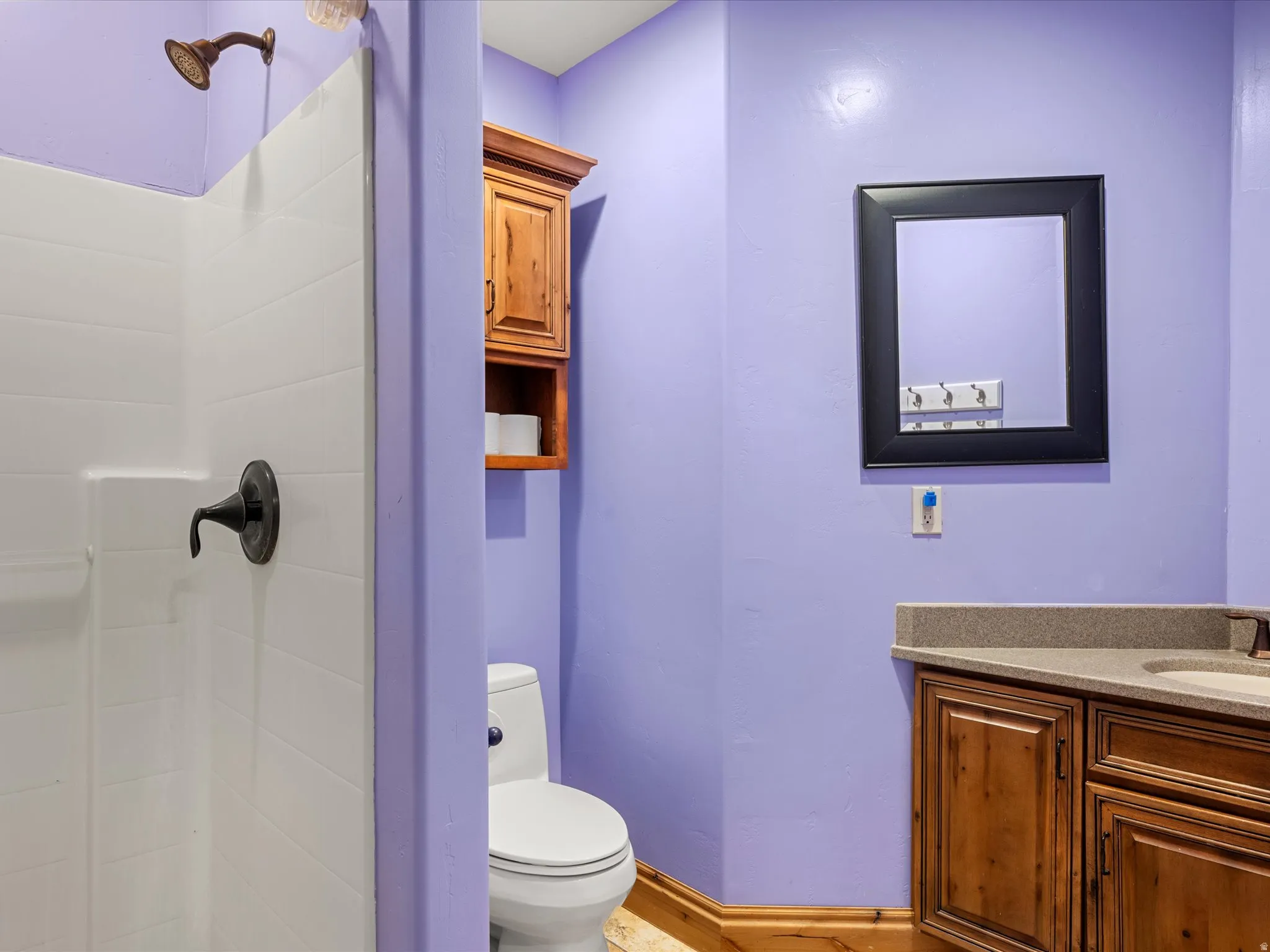 Bathroom featuring a white shower stall with bronze fixtures, a vanity with wood-finish cabinetry, a light-toned countertop, and a framed mirror