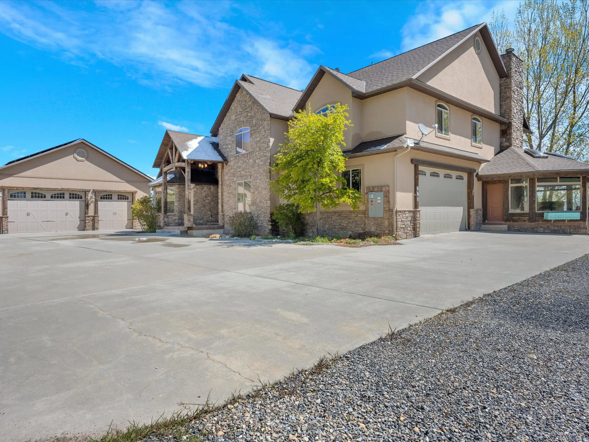 Stately stone and stucco exterior featuring multiple gables, an attached garage, a detached garage, a covered front entry, and a gravel driveway