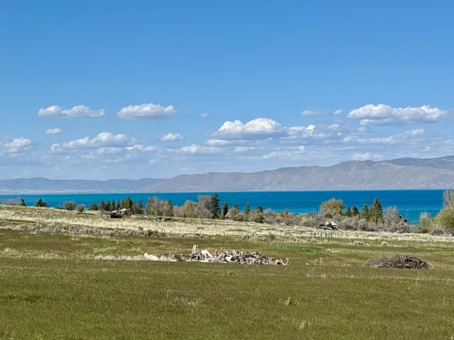 Expansive undeveloped land featuring a broad field, natural foliage, distant mountain ranges, and a large body of water