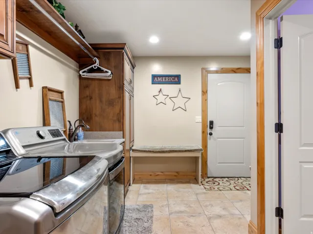 Basement laundry room.Dedicated utility space featuring wood-finish cabinetry, a utility sink with an integrated countertop, recessed lighting, and tile flooring