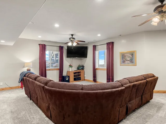 Carpeted living area featuring recessed lighting, a ceiling fan, and multiple windows with wood trim