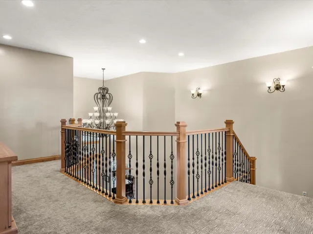 Upper-level landing featuring a wood and wrought iron railing, recessed lighting, and wall-mounted sconces