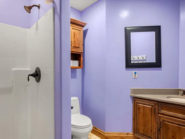 Bathroom featuring a white shower stall with bronze fixtures, a vanity with wood-finish cabinetry, a light-toned countertop, and a framed mirror