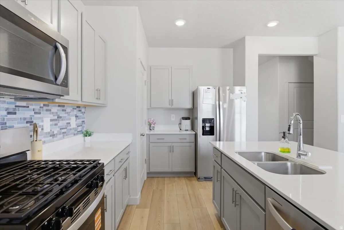 Kitchen featuring light gray cabinetry, stainless steel appliances, light wood-finish flooring, a mosaic tile backsplash, and white countertops