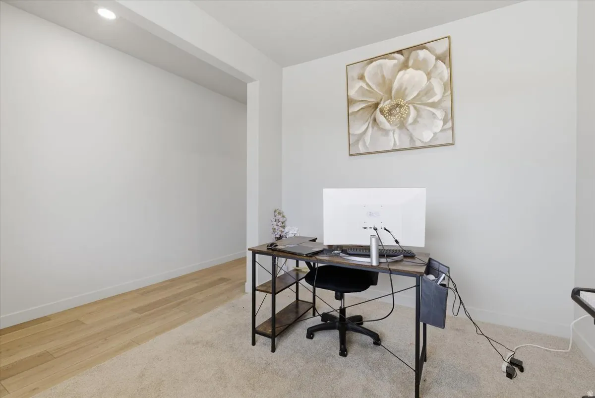 Spacious room featuring light-toned walls, recessed lighting, and a blend of light wood-finish flooring and plush carpeting