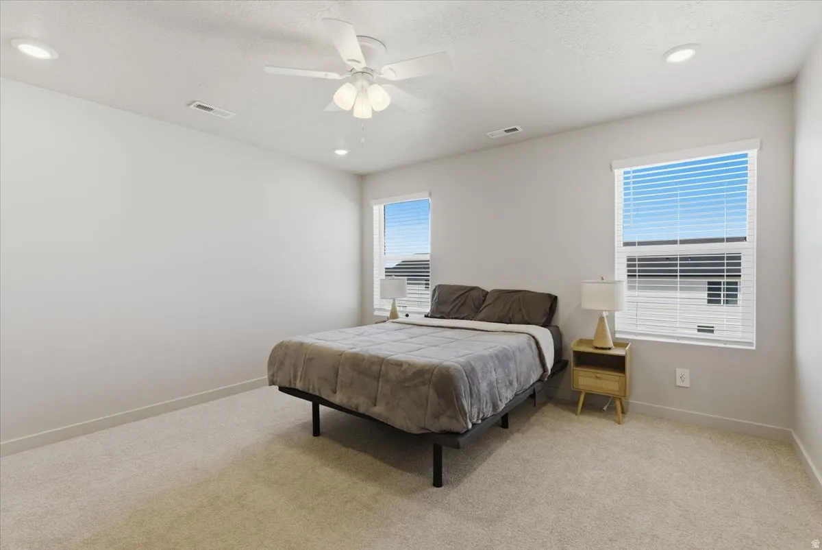 Spacious room featuring neutral carpeting, two windows with horizontal blinds, and a ceiling fan with integrated lighting