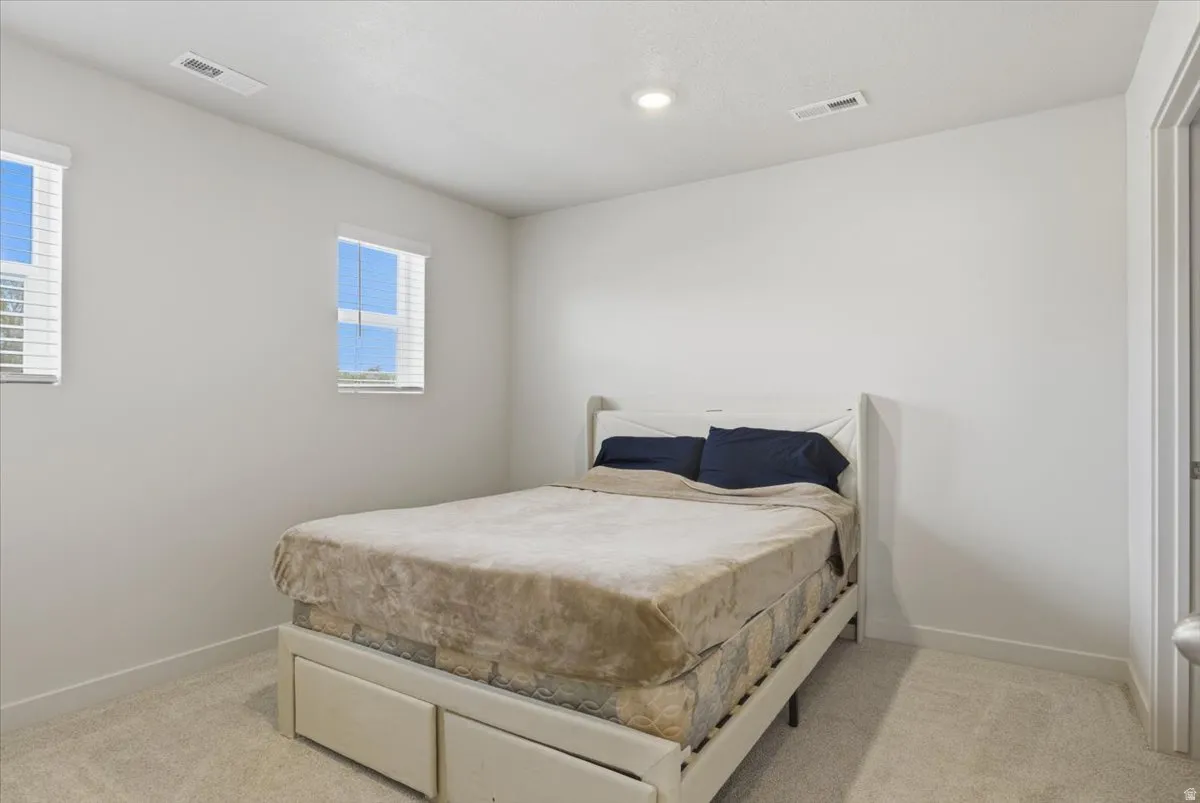 Carpeted interior room featuring two windows with horizontal blinds, a white door frame, white baseboards, and a ceiling-mounted light fixture