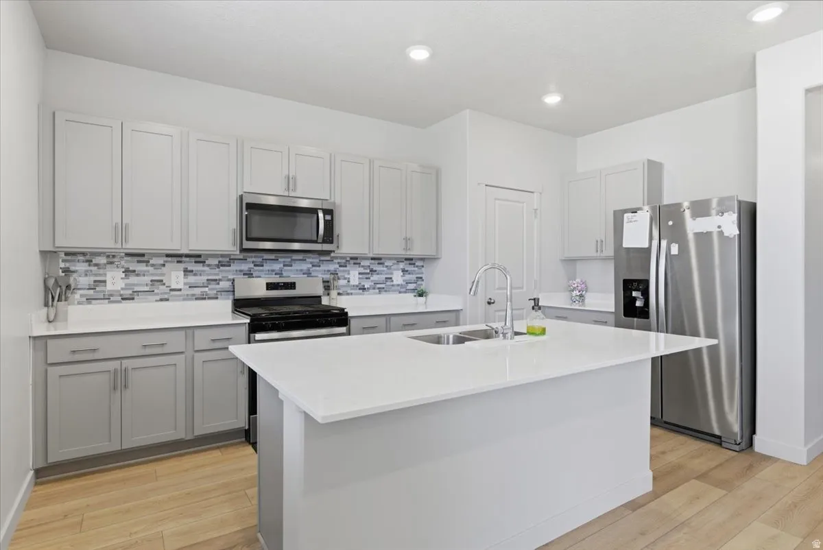 Kitchen featuring light gray cabinetry, white countertops, stainless steel appliances, a mosaic tile backsplash, and wood-finish flooring