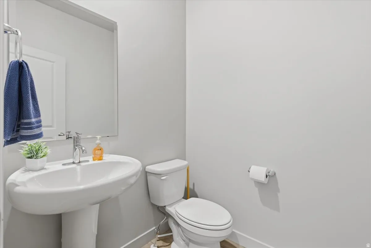 Powder room featuring a pedestal sink with chrome faucet, a rectangular wall-mounted mirror, and a white toilet