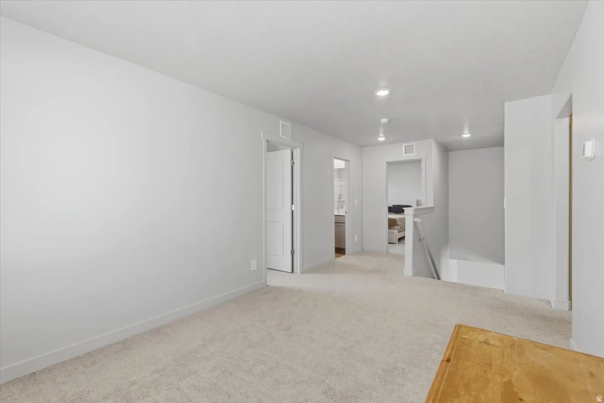 Spacious carpeted room featuring light gray walls, recessed lighting, and white trim