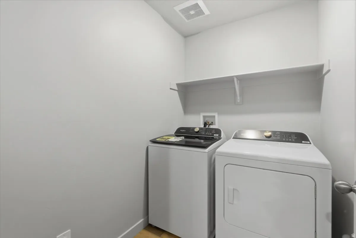 Dedicated laundry space featuring a white wall shelf, built-in ventilation, and wood-finish flooring