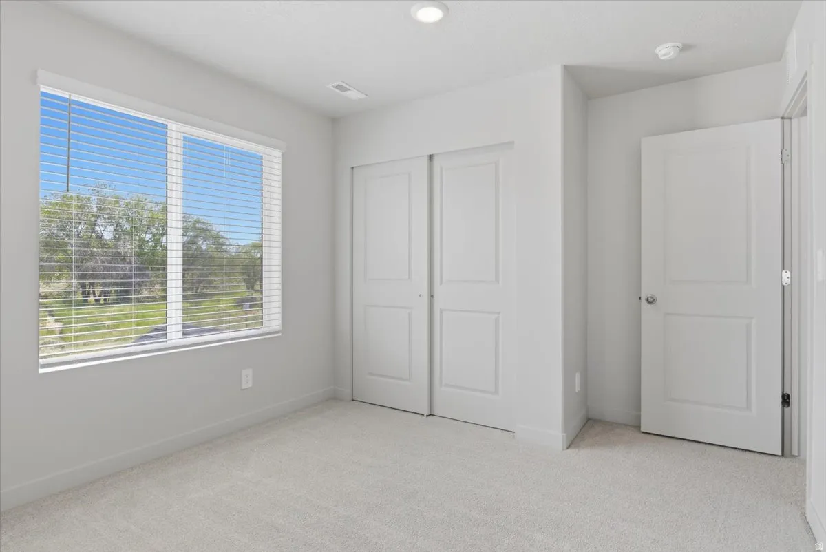 Bright bedroom featuring a large window with horizontal blinds, neutral carpet flooring, sliding double-panel closet doors, and recessed ceiling lighting
