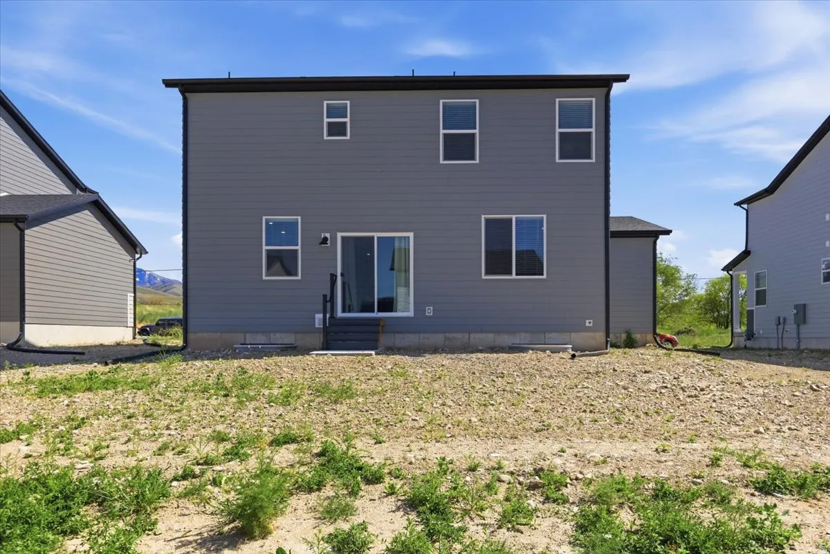 Rear exterior featuring gray horizontal siding, black trim, and a sliding glass door with exterior lighting