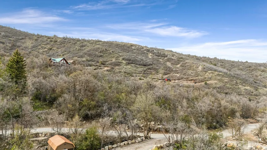Mountainous terrain with a remote cabin featuring a green roof, natural wood siding, and surrounding evergreen trees