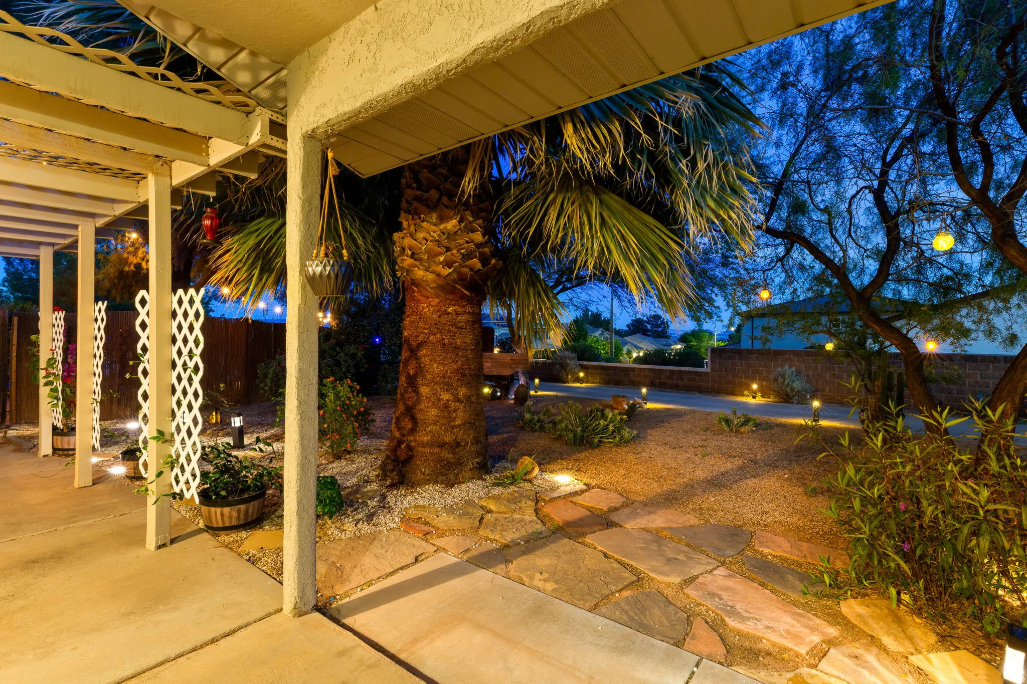 Expansive patio and low-maintenance landscape featuring a concrete patio, stone pathway, mature palm tree, and illuminated perimeter