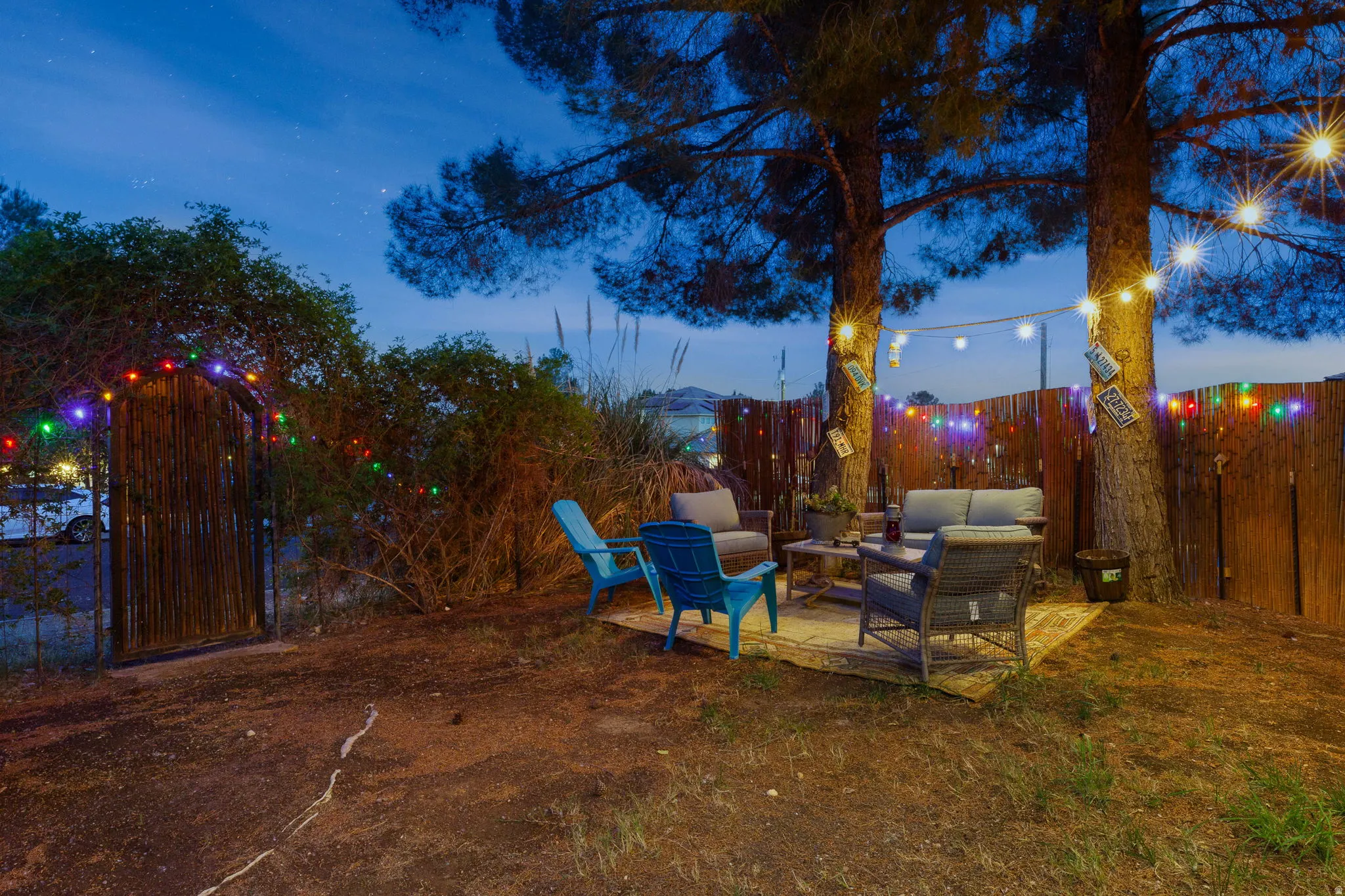 Outdoor patio space featuring string lighting, a wooden privacy fence, mature trees, and a decorative gate