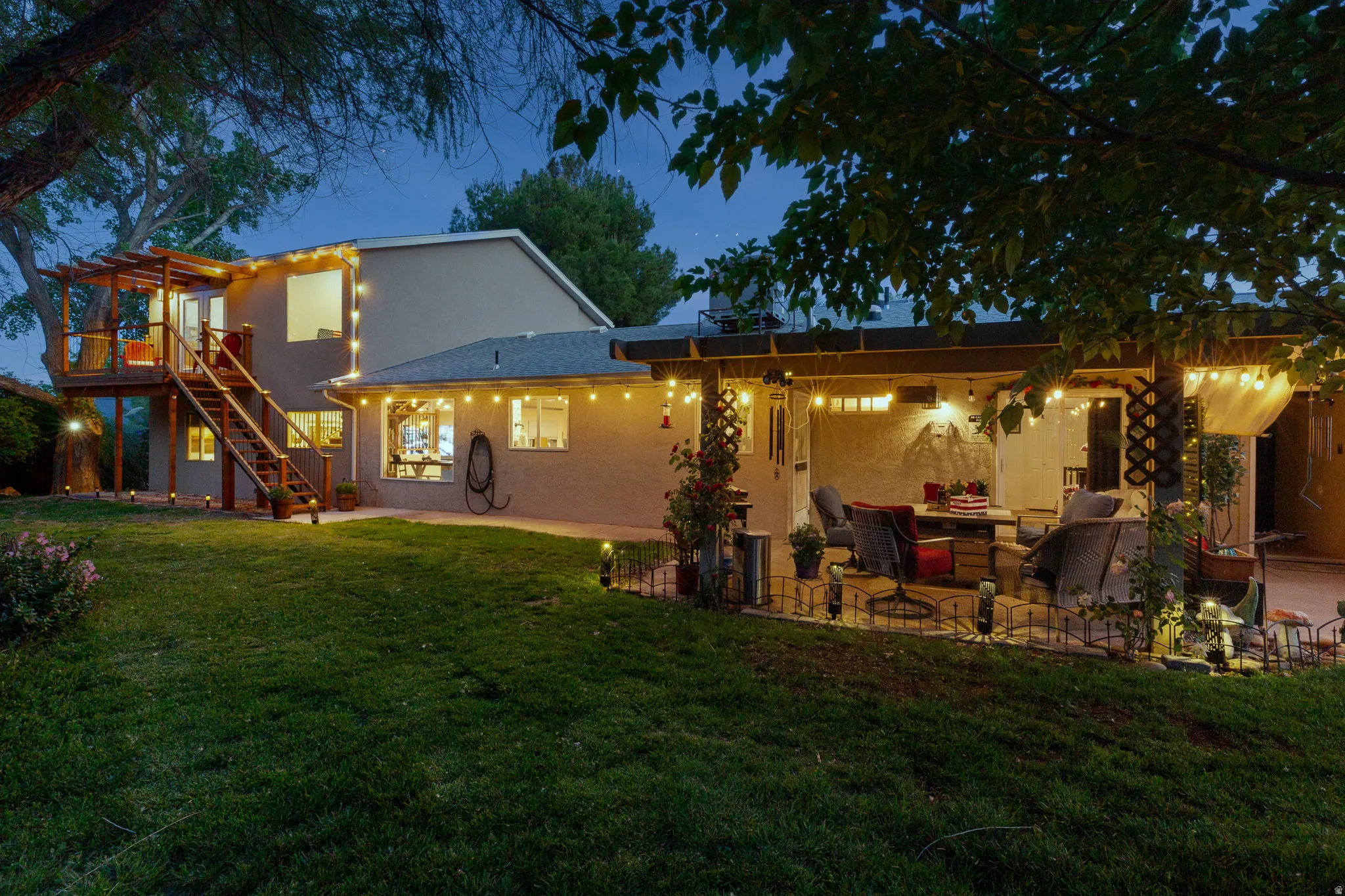 Expansive backyard featuring a tiered wooden deck with pergola, an open-air patio with a pergola, ground-level windows, and a stucco exterior