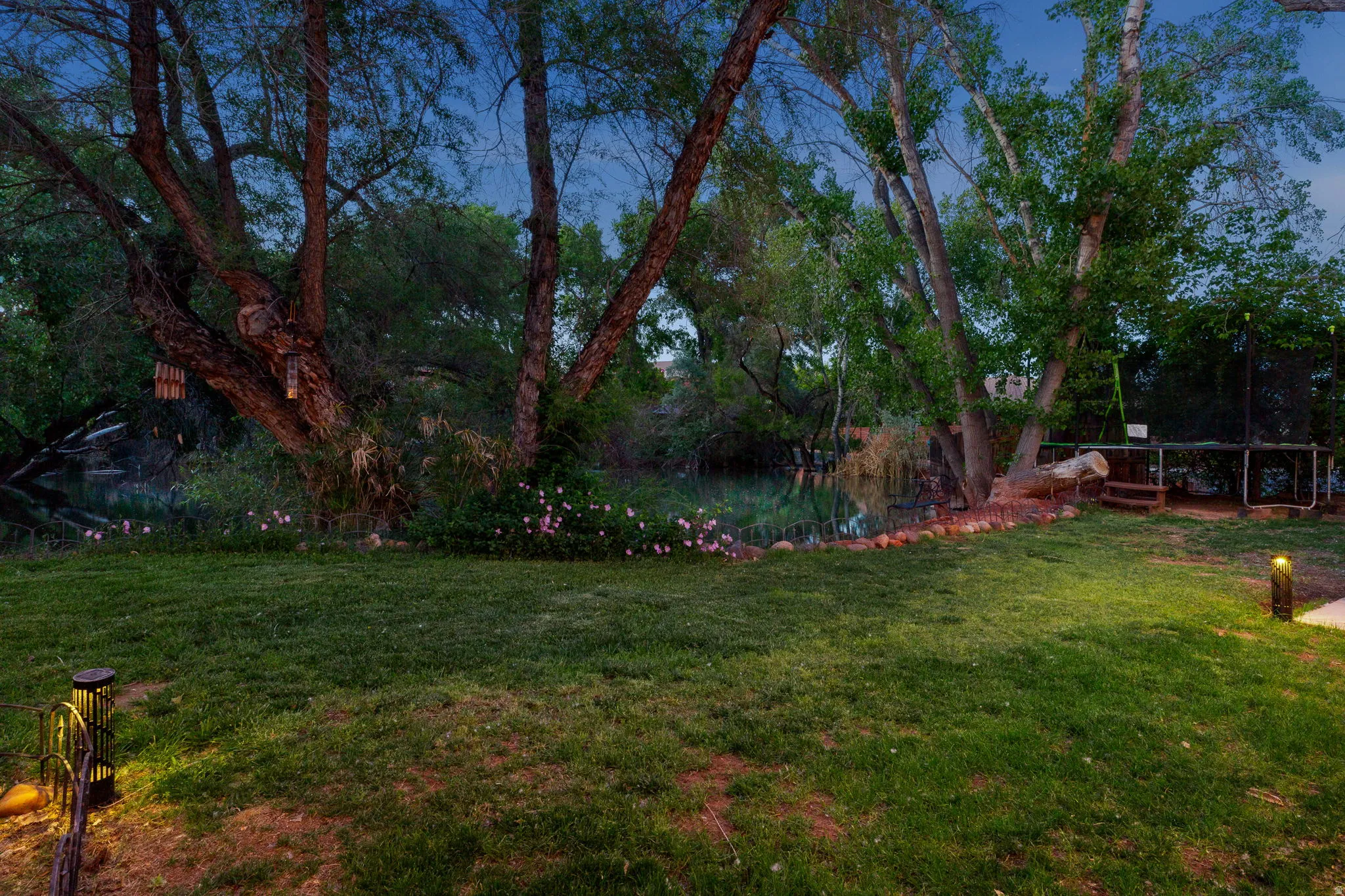 Expansive backyard featuring mature trees, a manicured lawn, and a natural water feature