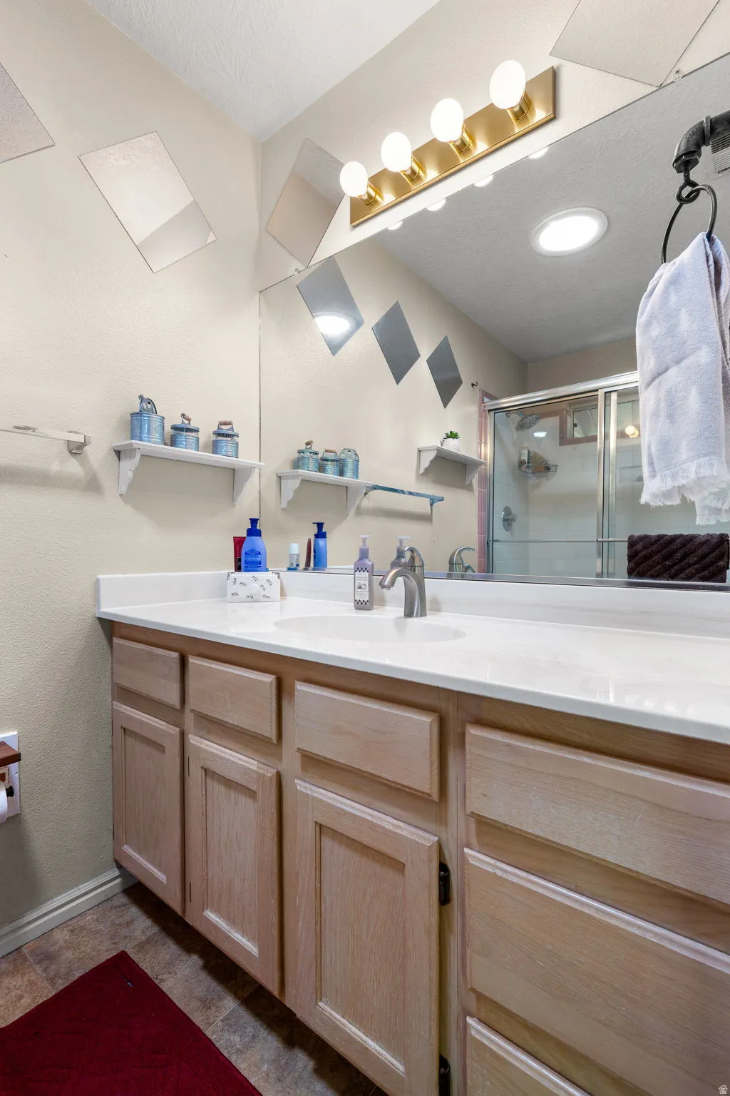 Bathroom vanity with a light wood-finish cabinetry, a white countertop, and a single basin sink