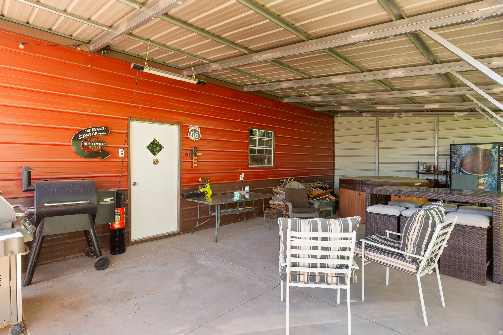 Covered outdoor patio area featuring a concrete slab, a corrugated metal roof structure, and a red corrugated metal wall