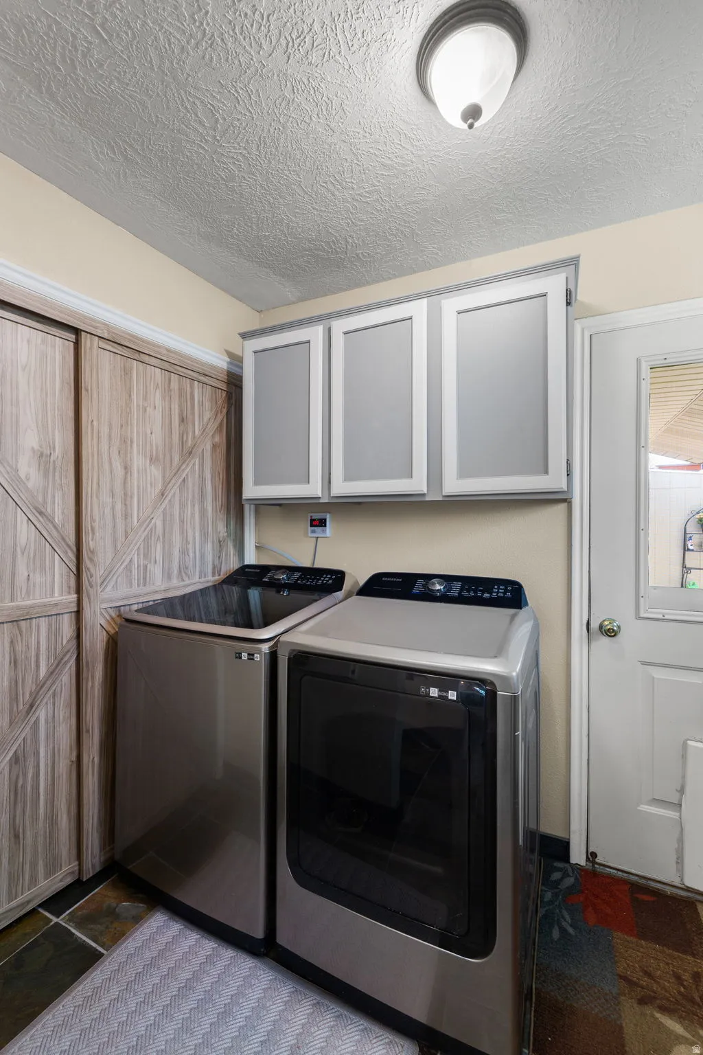 Laundry area featuring upper cabinetry, multi-toned slate-style flooring, and wood-look sliding closet doors