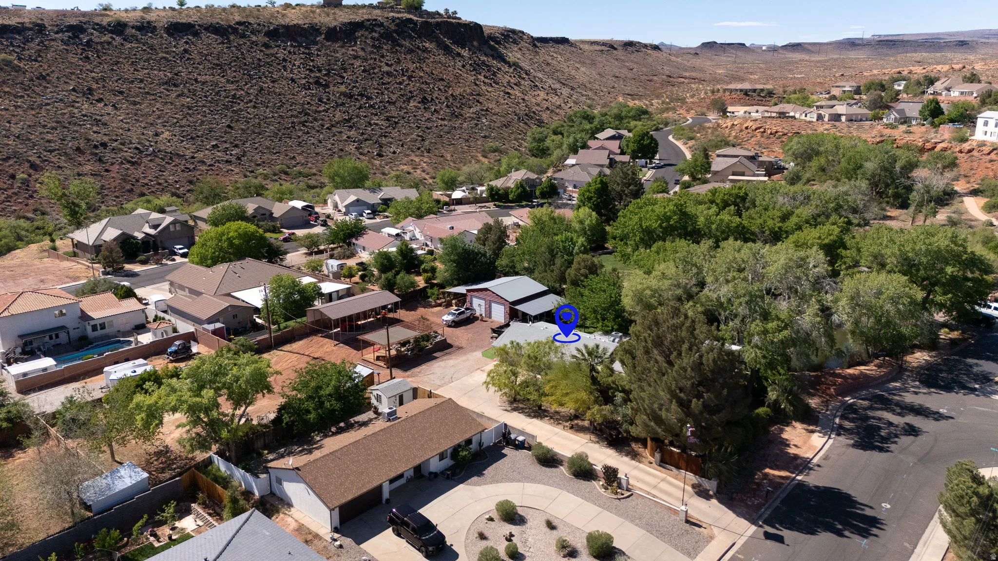 Residential neighborhood featuring diverse housing styles, mature trees, a backdrop of natural rock formations, and clear skies