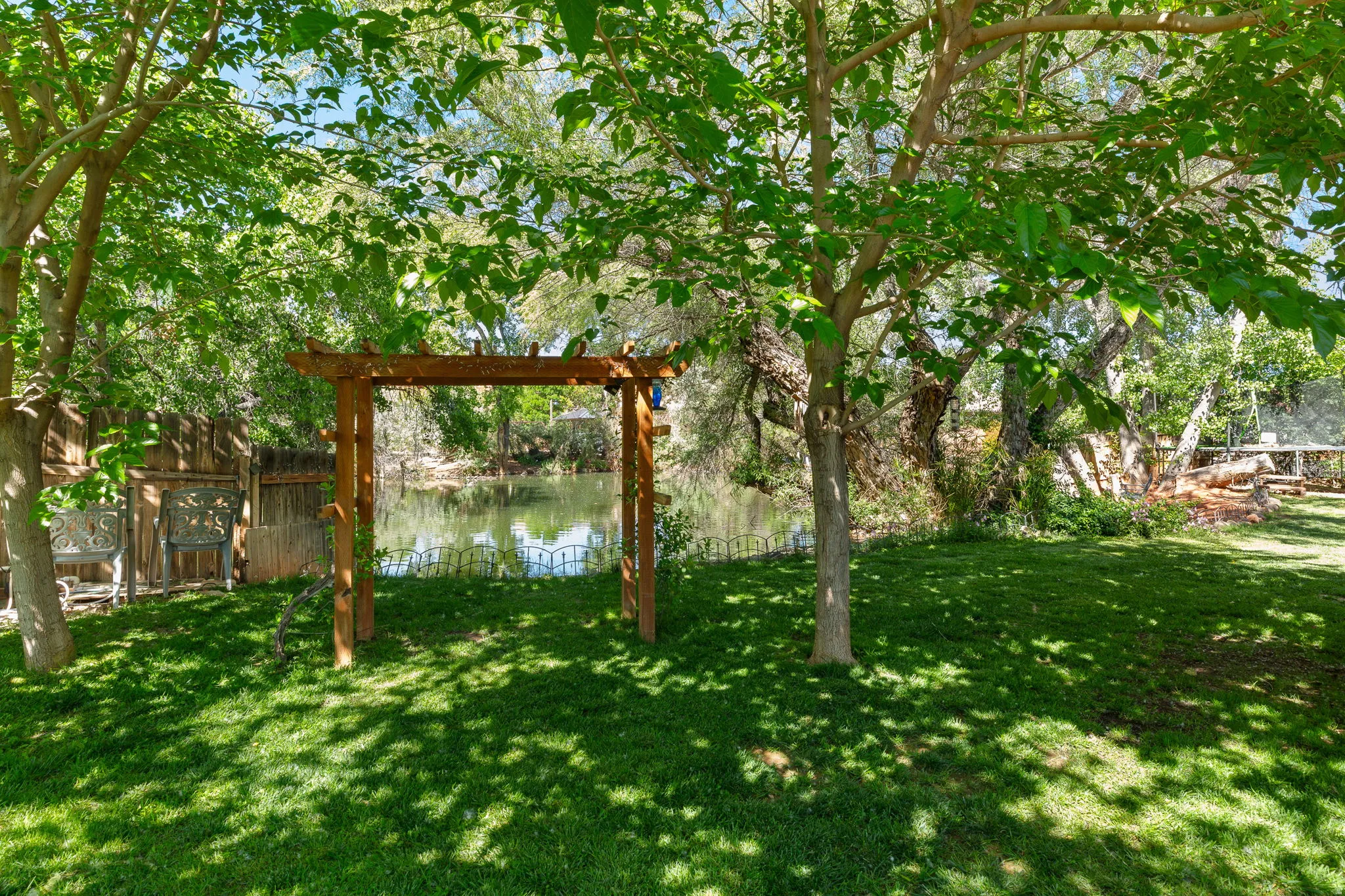 Expansive backyard featuring a manicured lawn, mature trees, and a wooden arbor leading to a water feature