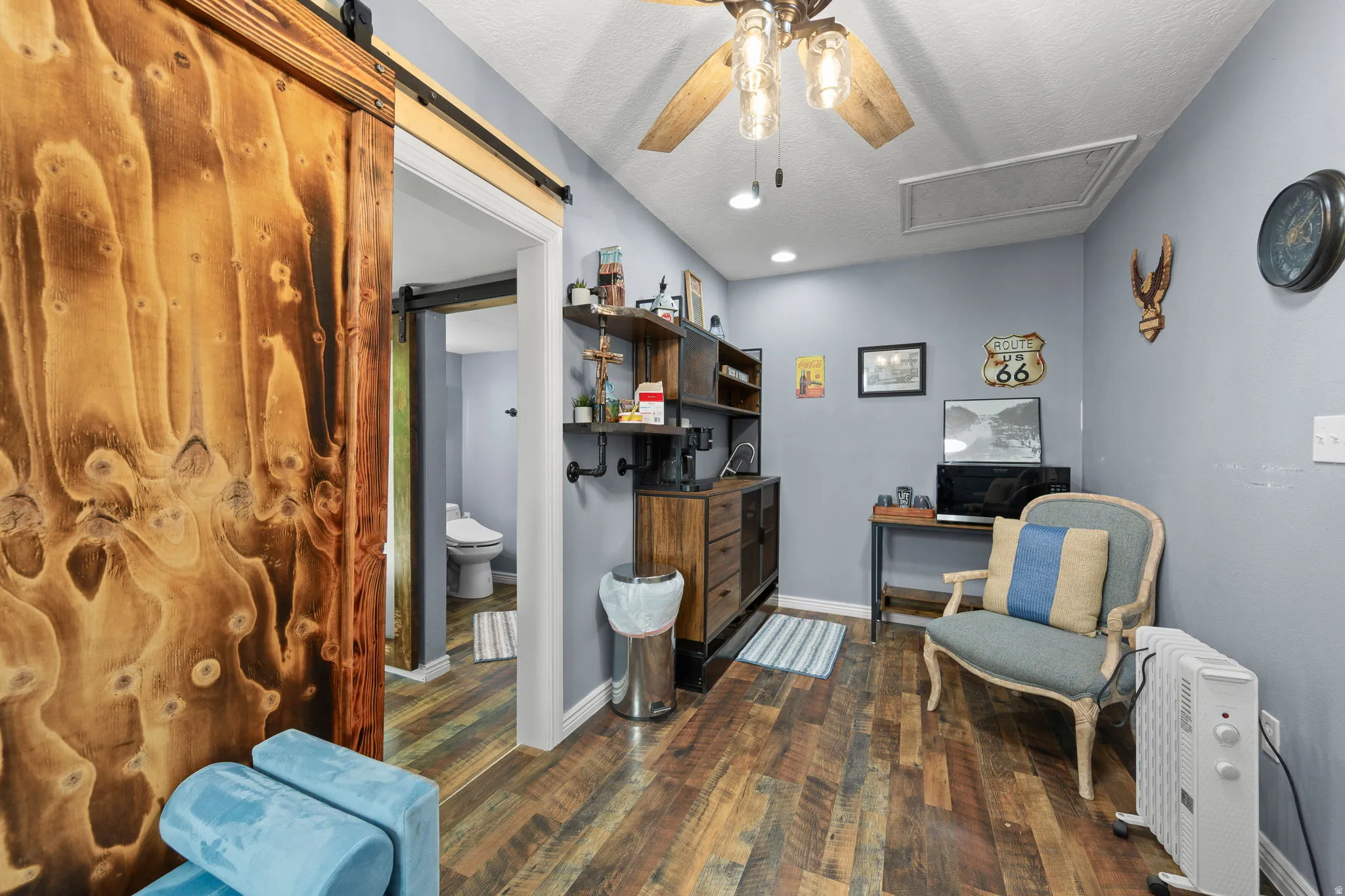 Room featuring wood-finish flooring, a rustic wood barn door with black hardware, and a ceiling fan with integrated lighting