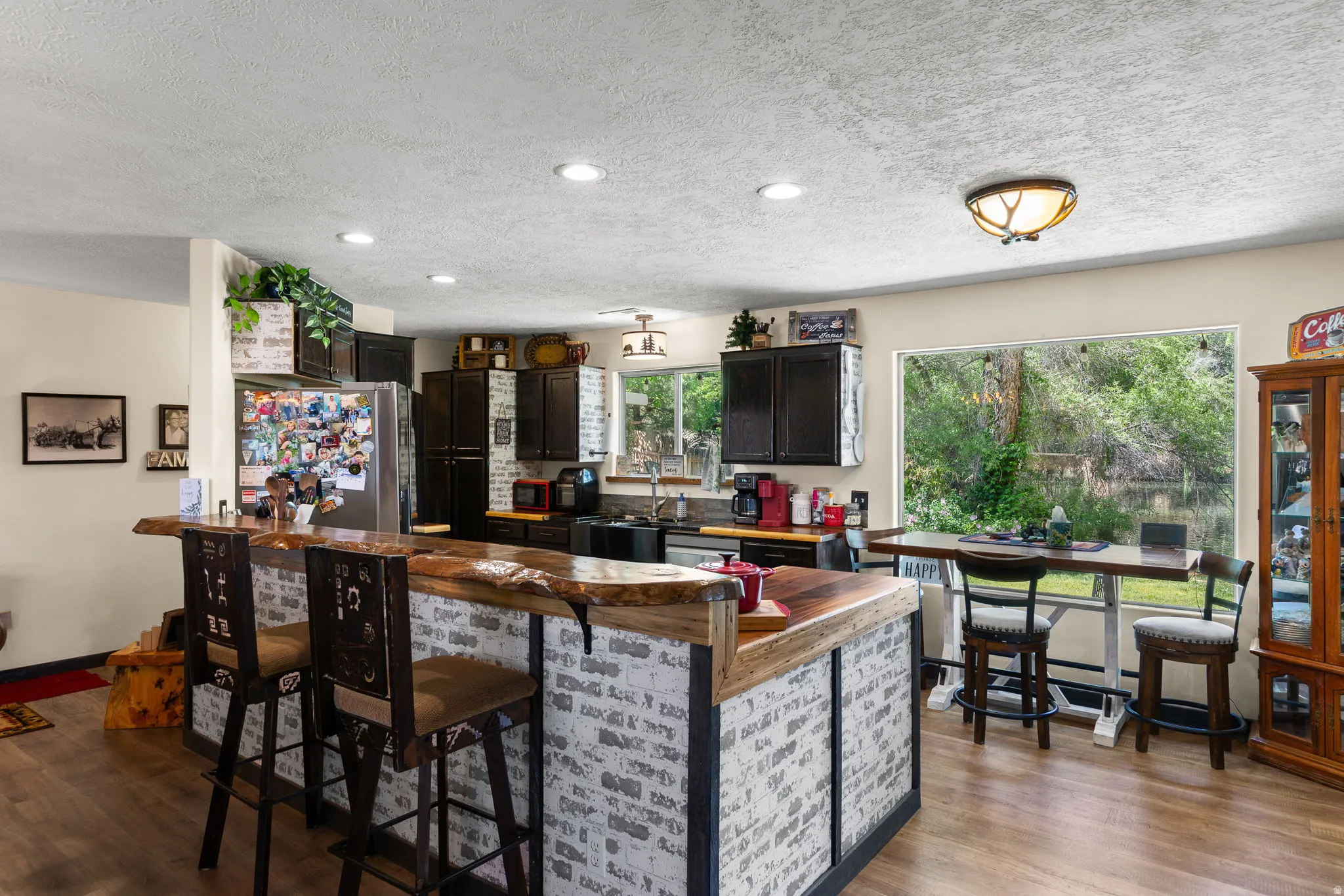 Kitchen featuring a live-edge wood island countertop, brick veneer island facade, dark wood-finish cabinetry, recessed lighting, and wood-finish flooring