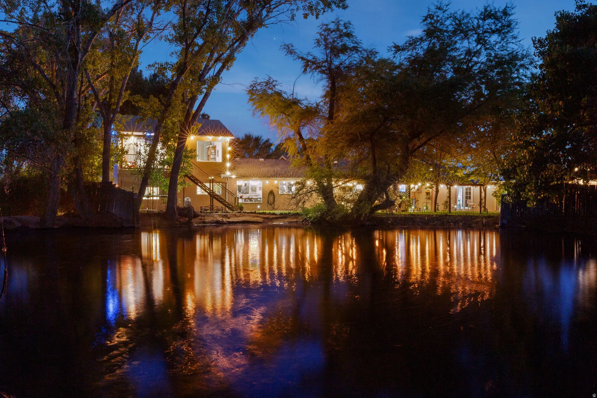 Waterfront property featuring a stucco exterior, multiple window designs, and outdoor string lighting
