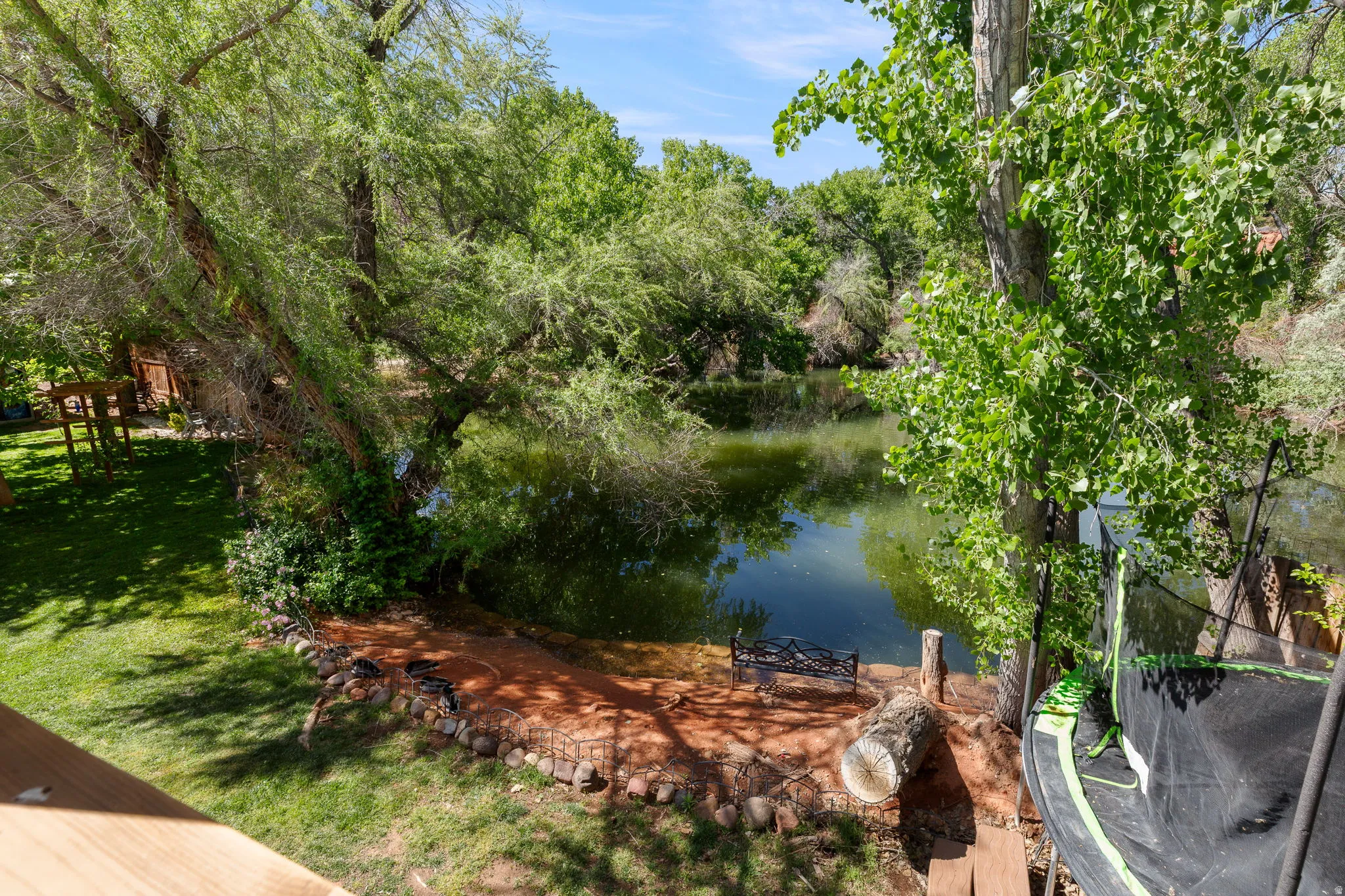 Expansive waterside landscape featuring mature trees, a manicured lawn, and a natural water feature