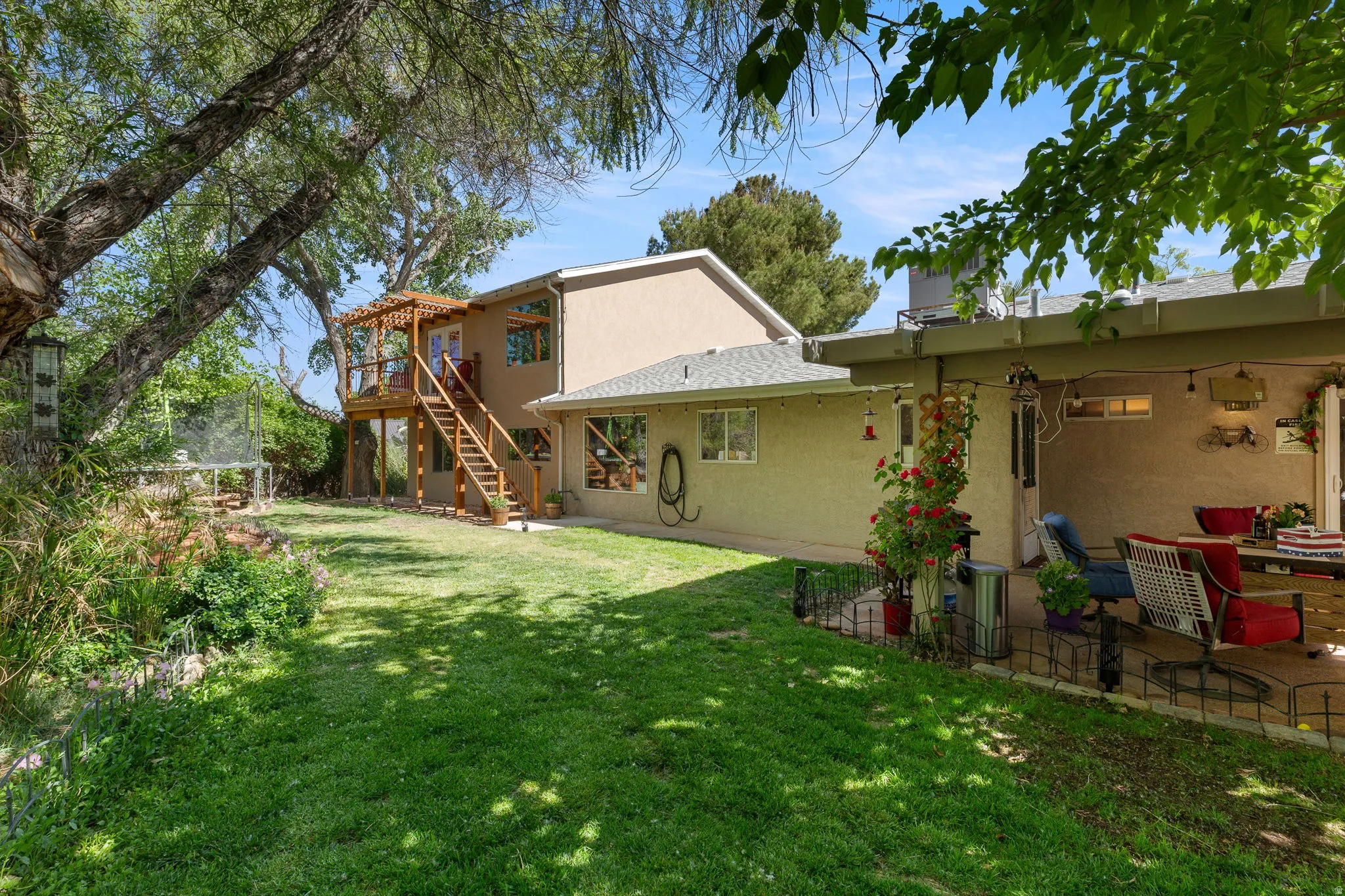 Expansive rear yard featuring a manicured lawn, established trees, and a covered patio area