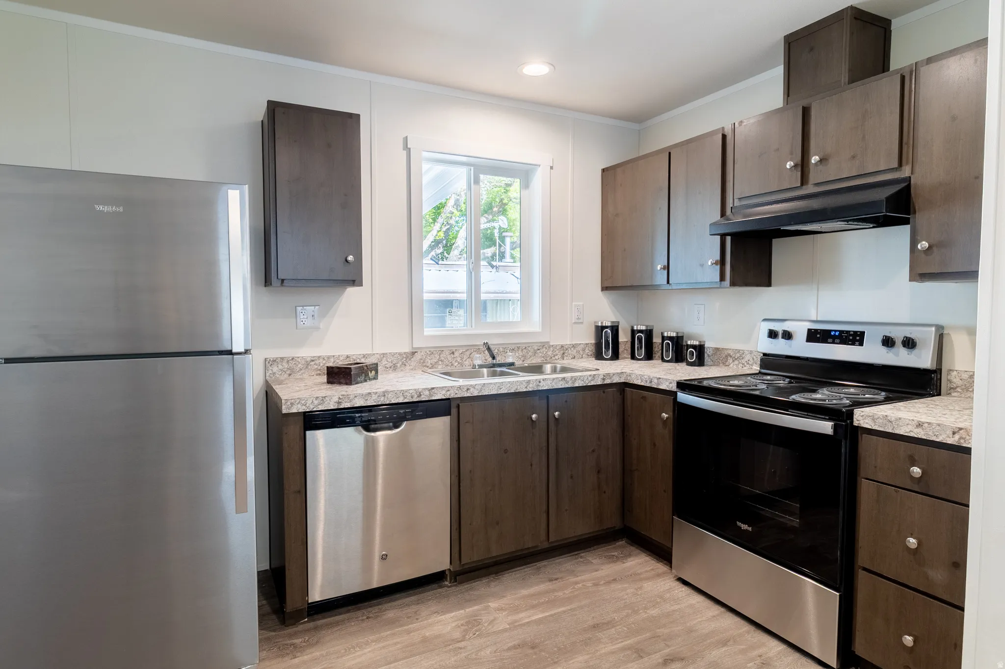 Kitchen with stainless steel appliances, light countertops, dark wood finish cabinetry, light wood finished floors, and crown molding