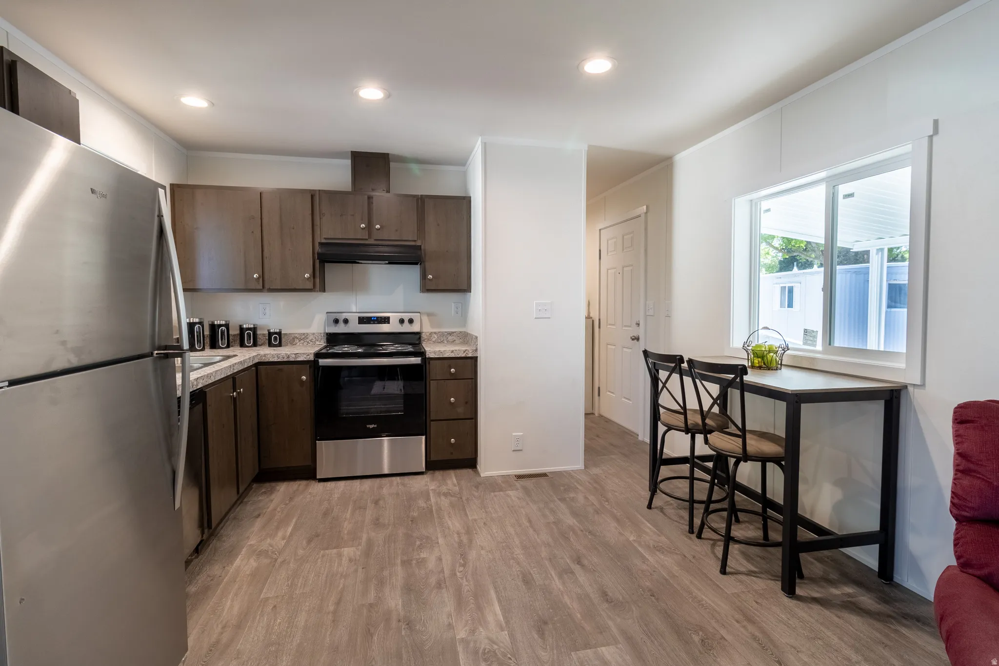 Kitchen with stainless steel appliances, dark wood finish cabinets, recessed lighting, light wood finished floors, and crown molding