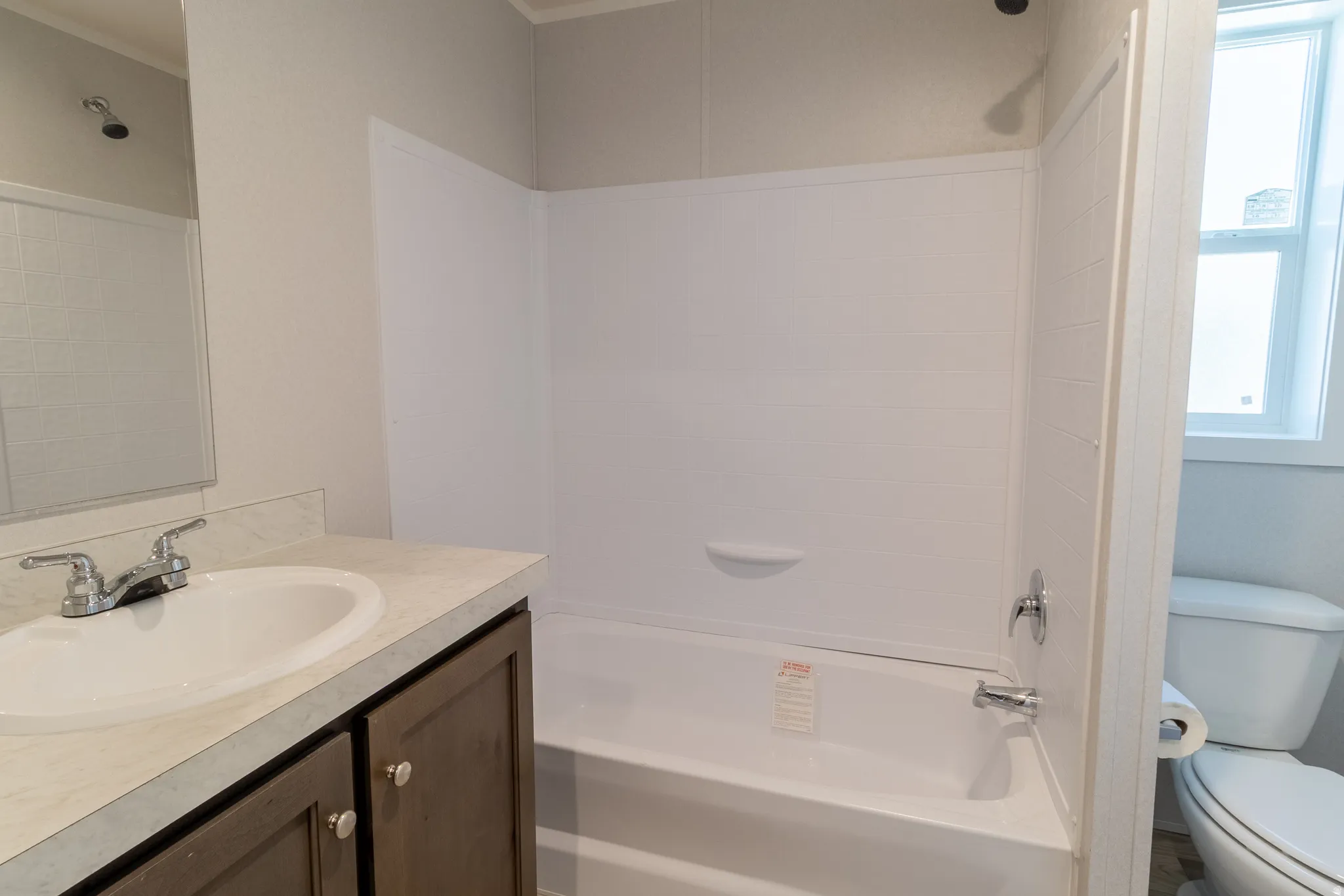 Bathroom featuring a white bathtub with integrated shower, a vanity with a white countertop and oval sink, dark wood-finish cabinetry, and chrome fixtures