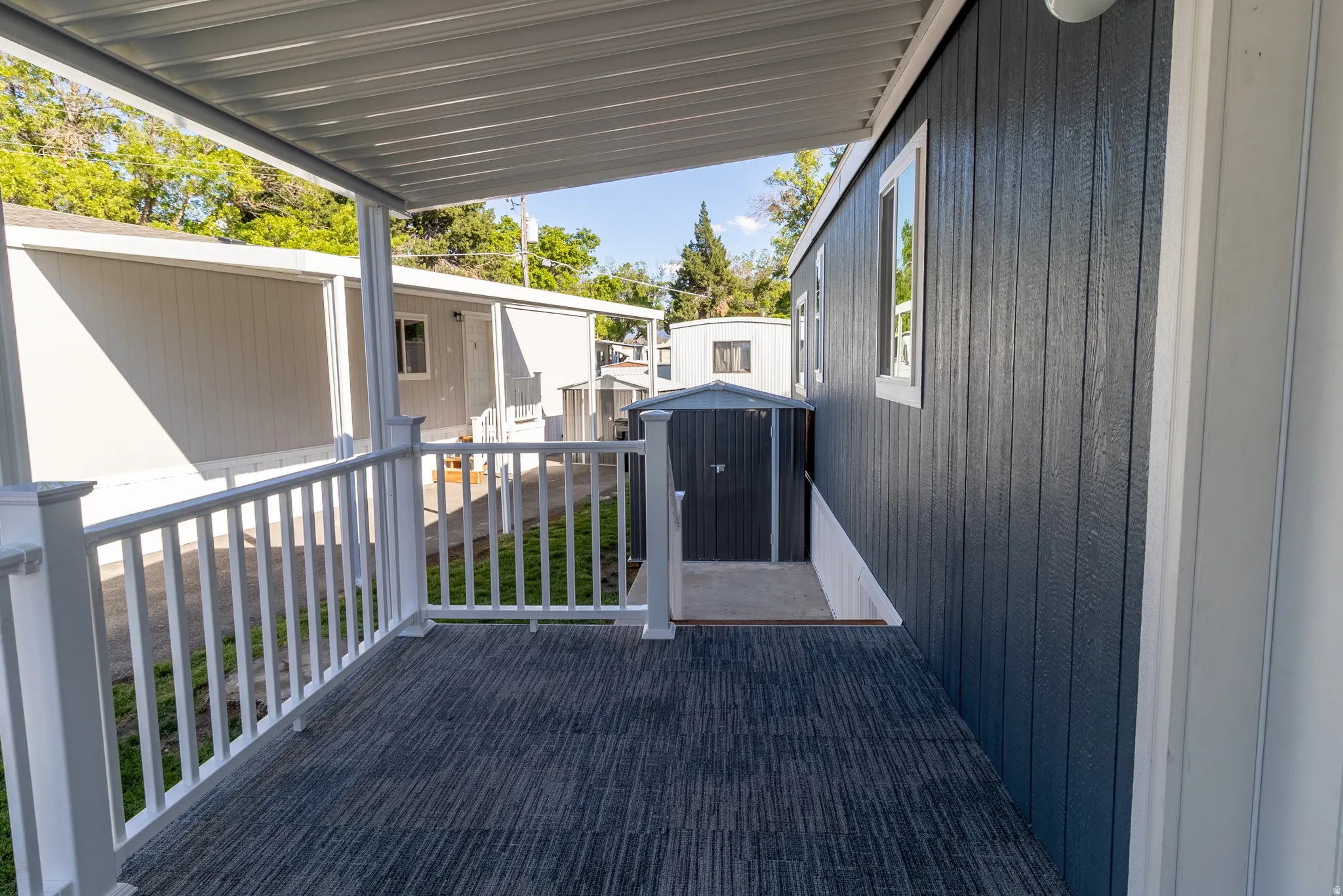 Covered outdoor porch with patterned flooring, white railing, and dark blue vertical siding