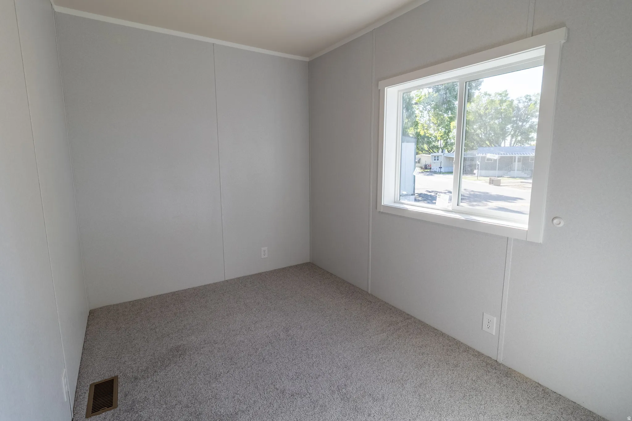 Carpeted interior space featuring light gray walls, white trim, and a window with white casing