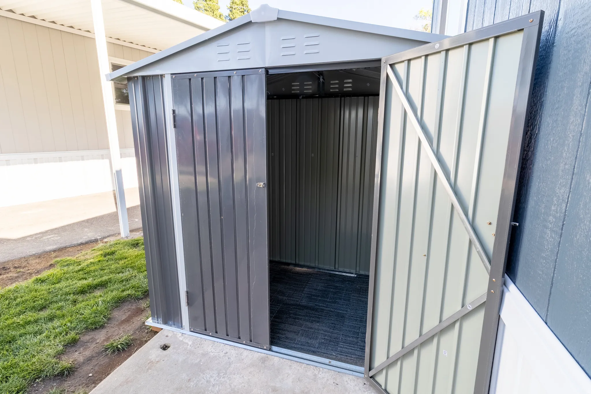 Compact metal storage shed with a gable roof, double doors, and a concrete pad