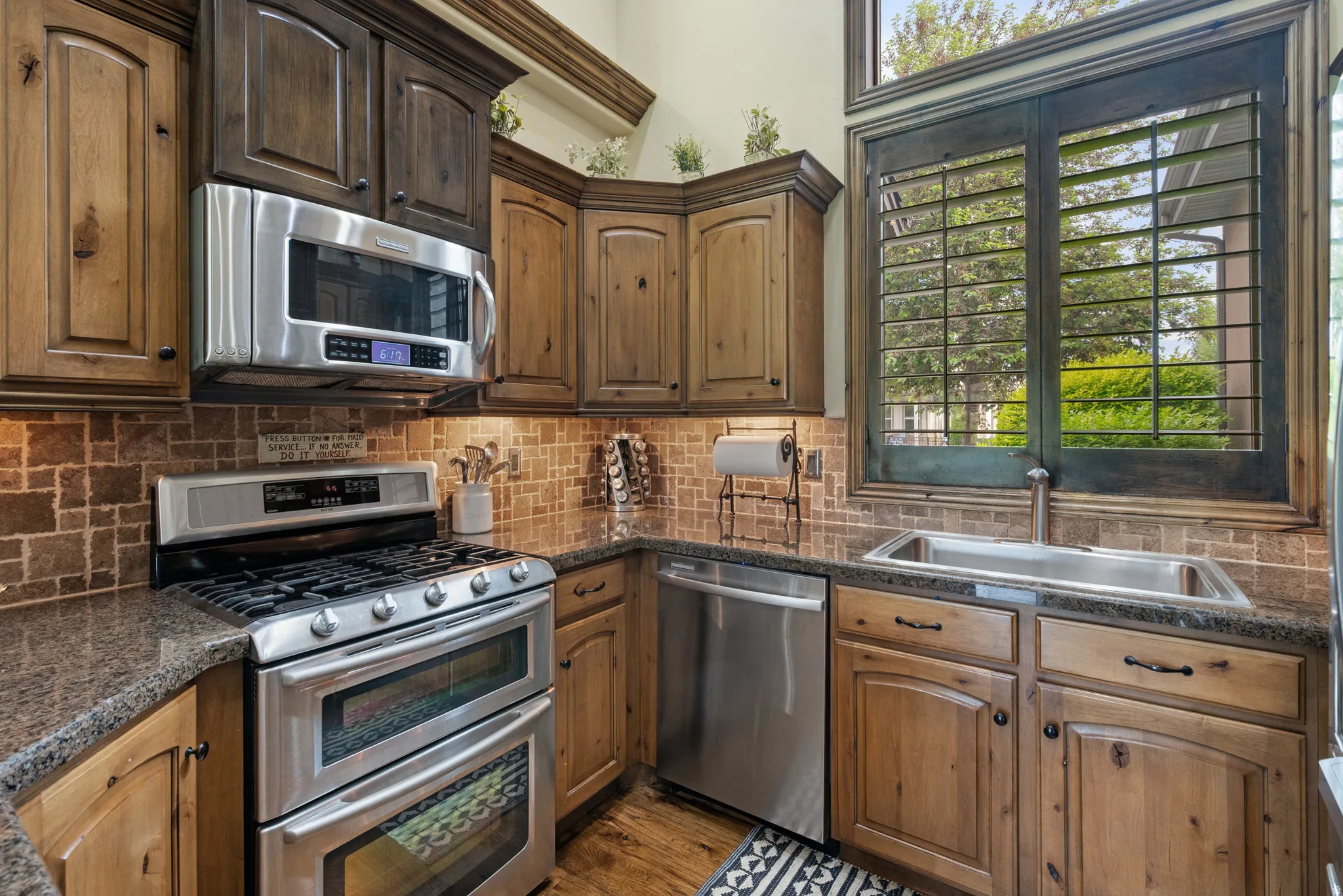 Kitchen featuring stainless steel appliances, dual-tone cabinetry, tiled backsplash, and stone-finish countertops