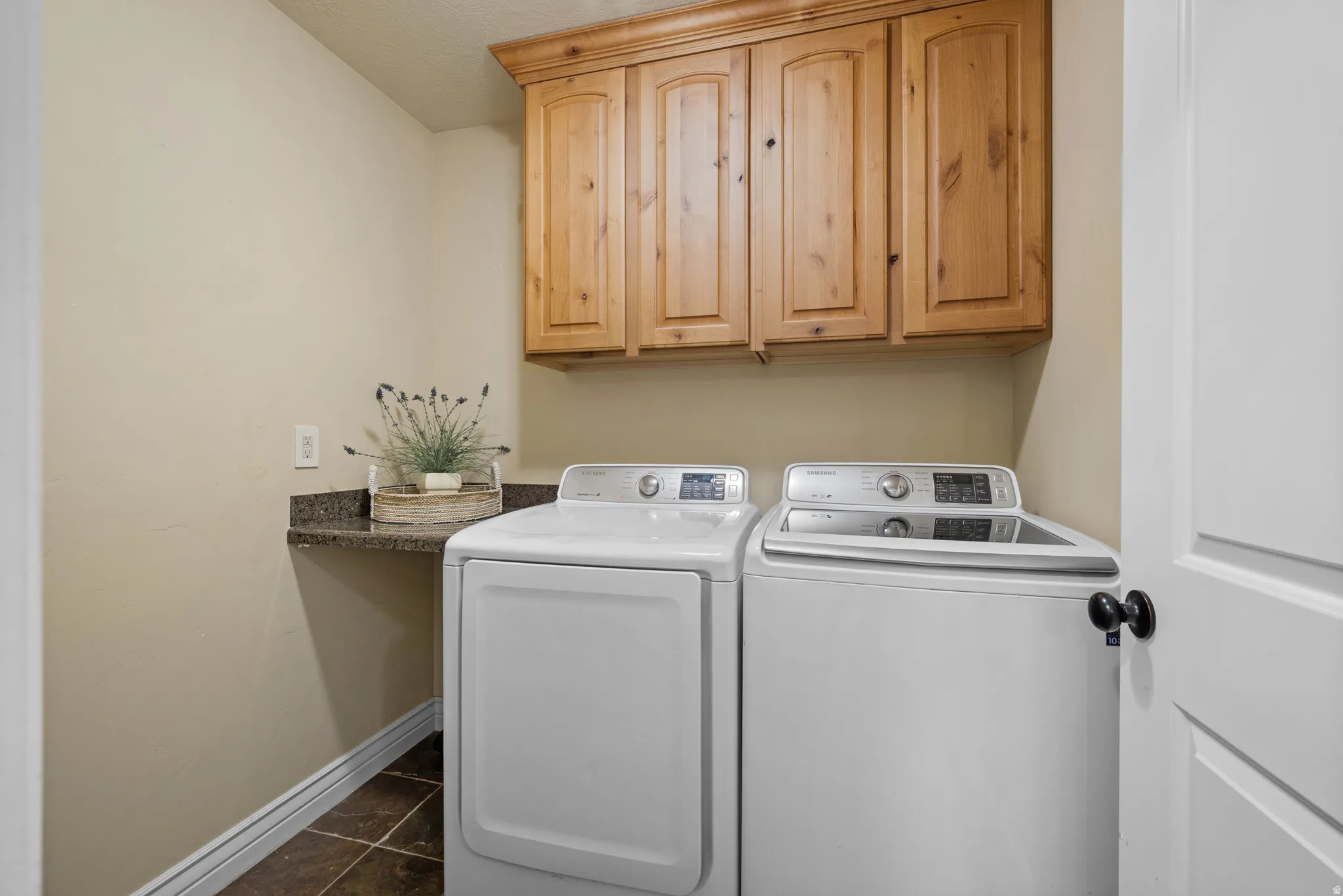 Dedicated laundry area featuring upper wood cabinetry, a dark countertop, and durable tile flooring