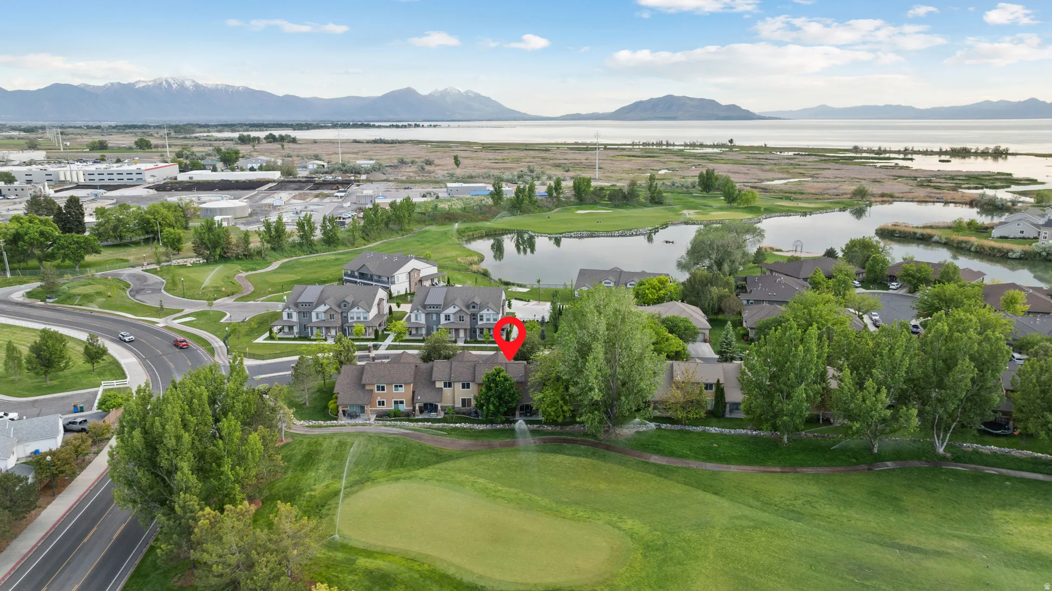 Aerial perspective showcasing a residential area bordered by a golf course, bodies of water, and distant mountains